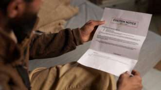 A man, shot from over the shoulder, holds an eviction notice. | Pressmaster | Dreamstime.com