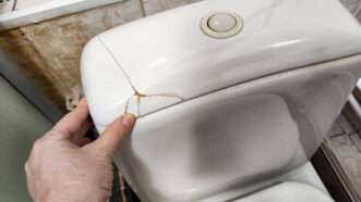 A plumber's hand examines a crack in the lid of a toilet tank. | Krivosheina Elena | Dreamstime.com