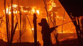 A firefighter fights the flames consuming a building in the background |  Andrew Silk/ZUMAPRESS/Newscom