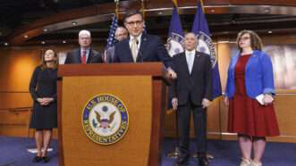 Speaker of the House Mike Johnson stands at a podium with people standing behind him | CNP/AdMedia/Newscom