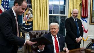 White House Staff Secretary Will Scharf hands an executive order to President Donald Trump for him to sign. Trump sits behind the Resolute Desk in the Oval Office, as Commerce Secretary Howard Lutnick stands nearby. | Al Drago - Pool via CNP/picture alliance / Consolidated News Photos/Newscom