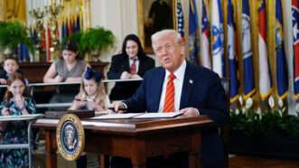 President Donald Trump sits at a desk before signing an executive order calling for the abolition of the Department of Education, as school children sit at the desks in the background. | Sipa USA/Newscom