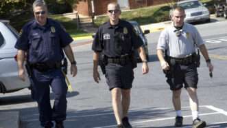 Three police officers, in various degrees of uniform, walk in a line. | Thomas Carter | Dreamstime.com