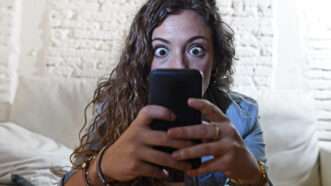 A woman stares at her cell phone, wide-eyed as if in shock. | Ocusfocus | Dreamstime.com