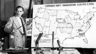 Joseph McCarthy standing in front of a map of Communist Party organizations across the United States in 1950 | Photo: Sen. Joseph McCarthy before Senate committee, 1950s; CSU Archives/Everett Collection/Alamy