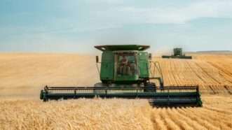 A green combine moves across a field | Photo by Darla Hueske on Unsplash