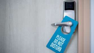 A closed hotel room door, with a blue sign on the handle that says "Please Do Not Disturb." | Ezthaiphoto | Dreamstime.com