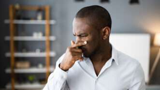 A man covers his nose, as if experiencing a terrible smell or something painful. | Andrey Popov | Dreamstime.com