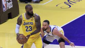 LeBron James holding a basketball, with his back turned to Stephen Curry, who is crouched down low guarding LeBron. | Ariana Ruiz/ZUMAPRESS/Newscom