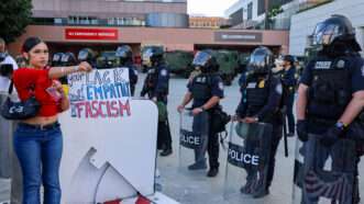 A woman holds a protest sign as Los Angeles police officers stand by in riot gear | Amy Katz/ZUMAPRESS/Newscom