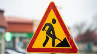 A triangular street sign depicting a human figure doing using a shovel, signifying there is road work taking place ahead. | Andery Moskvitin | Dreamstime.com