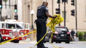 A Metropolitan Police Officer in Washington, D.C. sets up crime scene tape after the fatal shooting of two people outside a meeting of the American Jewish Committee. | BONNIE CASH/UPI/Newscom