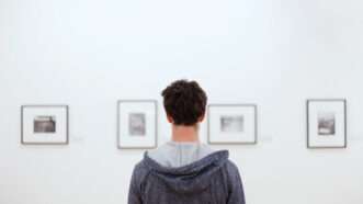 A man, seen from behind, looks at a series of artwork on display in a gallery. | Anyaberkut | Dreamstime.com