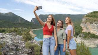 Three people taking a selfie with smart phone in the mountain on summer vacation | AntonioGuillem/Newscom