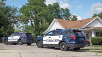 Two police SUVs sit parked outside a residential home. | Lawcain | Dreamstime.com