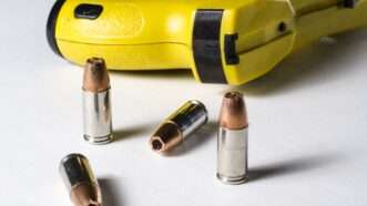 A Taser on its side, next to four hollow-point handgun bullets. | John Roman | Dreamstime.com