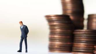 A tiny figurine of a businessman, slinking away from a stack of pennies. | Kineticimagery | Dreamstime.com