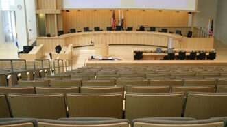 An empty city council meeting room, with stadium style chairs facing a dais at the front. | Stephen Coburn | Dreamstime.com