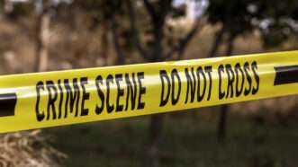 Yellow police tape, that reads "Crime scene, do not cross," in a wooded outdoor area. | Ruben Gasparyan | Dreamstime.com