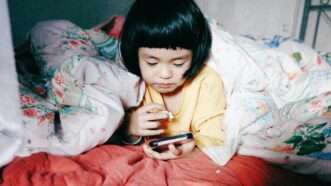 A young child using a smartphone | Photo by <a href="https://unsplash.com/@pandales?utm_content=creditCopyText&utm_medium=referral&utm_source=unsplash">Frank Ching</a> on <a href="https://unsplash.com/photos/a-little-girl-laying-in-bed-looking-at-a-cell-phone-KxN1IBdtxH0?utm_content=creditCopyText&utm_medium=referral&utm_source=unsplash">Unsplash</a>       