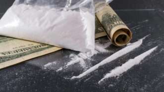 Big Bag and lines of cocaine on a glass surface with a rolled up one hundred dollar bill | DPST/Newscom