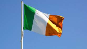 The flag of Ireland (with green, white, and orange stripes) flies atop a flagpole against a blue sky. | Diego Barbieri | Dreamstime.com