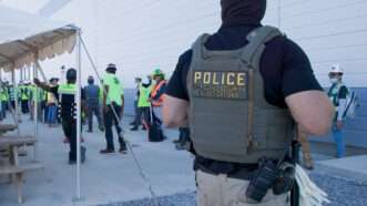 An ICE agent stands outside a building with several people wearing bright green seen in the background | U.S. ICE/UPI/Newscom