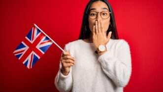 A young woman holds a U.K. flag in one hand while using the other to cover her mouth. | Aaron Amat | Dreamstime.com
