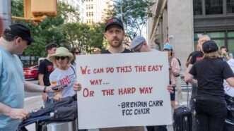 Protester holding Brendan Carr sign | Lev Radin/ZUMAPRESS/Newscom