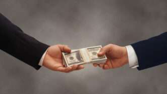Two businessmen pass a stack of $100 bills. | James Group Studios, Inc. | Dreamstime.com