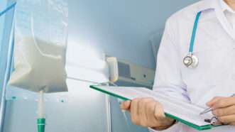 A doctor holds a clipboard by an I.V. pole. | Kanokwan Sangmontian | Dreamstime.com