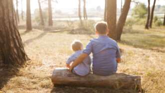 A brother sitting next to his younger sibling outdoors | ID 159417738 ©  Nazarii Karkhut | Dreamstime.com