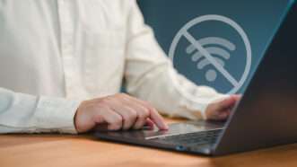 A man uses a laptop. A floating WiFi symbol with a circle and a line through it signifies an inability to connect to the internet. | Parin Kiratiatthakun | Dreamstime.com
