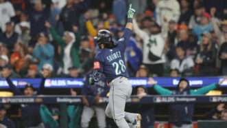 In a navy blue Seattle Mariners jersey, Eugenio Suárez points his hand in the air as he runs to first base, as Mariners players and fans celebrate in the background. | AARON JOSEFCZYK/UPI/Newscom