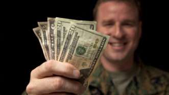 A man in U.S. Army fatigues happily holds up a handful of American money. | Elswarro | Dreamstime.com