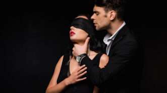 A blindfolded woman next to a man with his hand around her throat | DPST/Newscom
