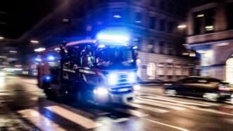 A fire truck driving fast through a city at night with its lights on. | Mino Surkala | Dreamstime.com