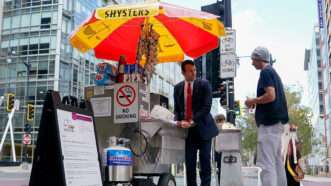 A man in a suit working at a hot dog cart | Photo: Isaac Stein, 31, at his hot dog stand, October 24, 2025; Elizabeth Frantz/Reuters