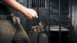 A prison guard holds a large ring of keys while walking by a darkened cell. | Fernando Gregory | Dreamstime.com