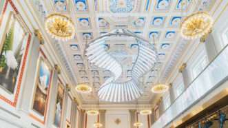 A bright and ornate room with paintings, chandeliers, and fancy ceiling tiles | Milken Center for Advancing the American Dream