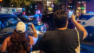 Two people holding phones and recording a police interaction | Photo: Andrew Leyden/Getty