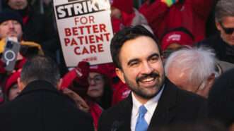 Zohran Mamdani surrounded by other people at a nurses' protest. One of them is holding up a sign that says "On strike for better patient care." | Derek French/ZUMAPRESS/Newscom