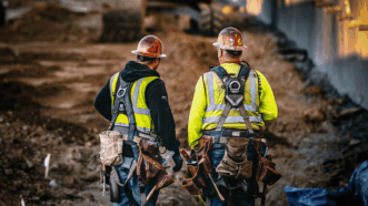 Two workers wearing construction equipment standing in front of an empty dirt area. | Photo: Daniel Mekis