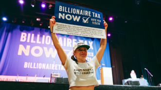 Photo of a woman holding up a sign that says "billionaire tax now" | David Pashaee/Middle East Images/StringersHub/Sipa USA/Newscom