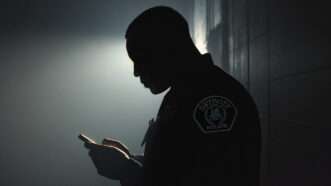A Detroit Police officer, in shadow, scrolls through a cell phone. | Illustration: Midjourney/Wikimedia Commons