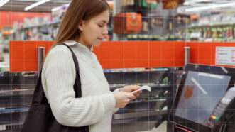 A woman shopping in a grocery store checks her receipt after using a self-checkout. | Envato