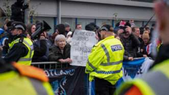 Police in Scotland at a protest outside the Cladhan Hotel. A demonstrator holds a sign that reads, "No more asylum seekers, give the homeless vets the beds instead." | Cameron Scott/ZUMAPRESS/Newscom