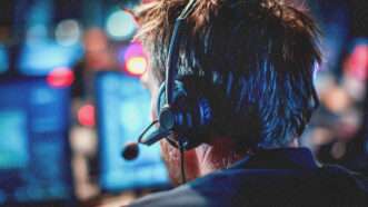 A 911 dispatcher with a headset sits in front of a screen. | Illustration: Midjourney