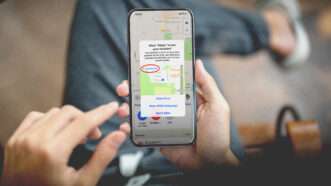 A person holds a cellphone displaying a request for permission to track the phone's location | Envato
