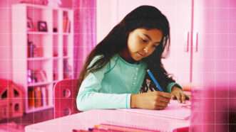 A young girl completes schoolwork at a desk. | Envato